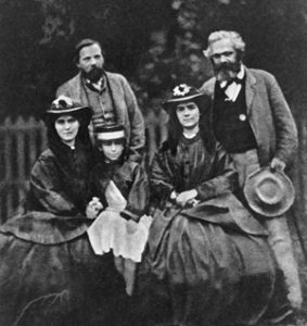 Rok 1864. Eleonora Marks siedząca między swoimi siostrami Laurą i Jenny. Za nimi stoją Fryderyk Engels i Karol Marks.